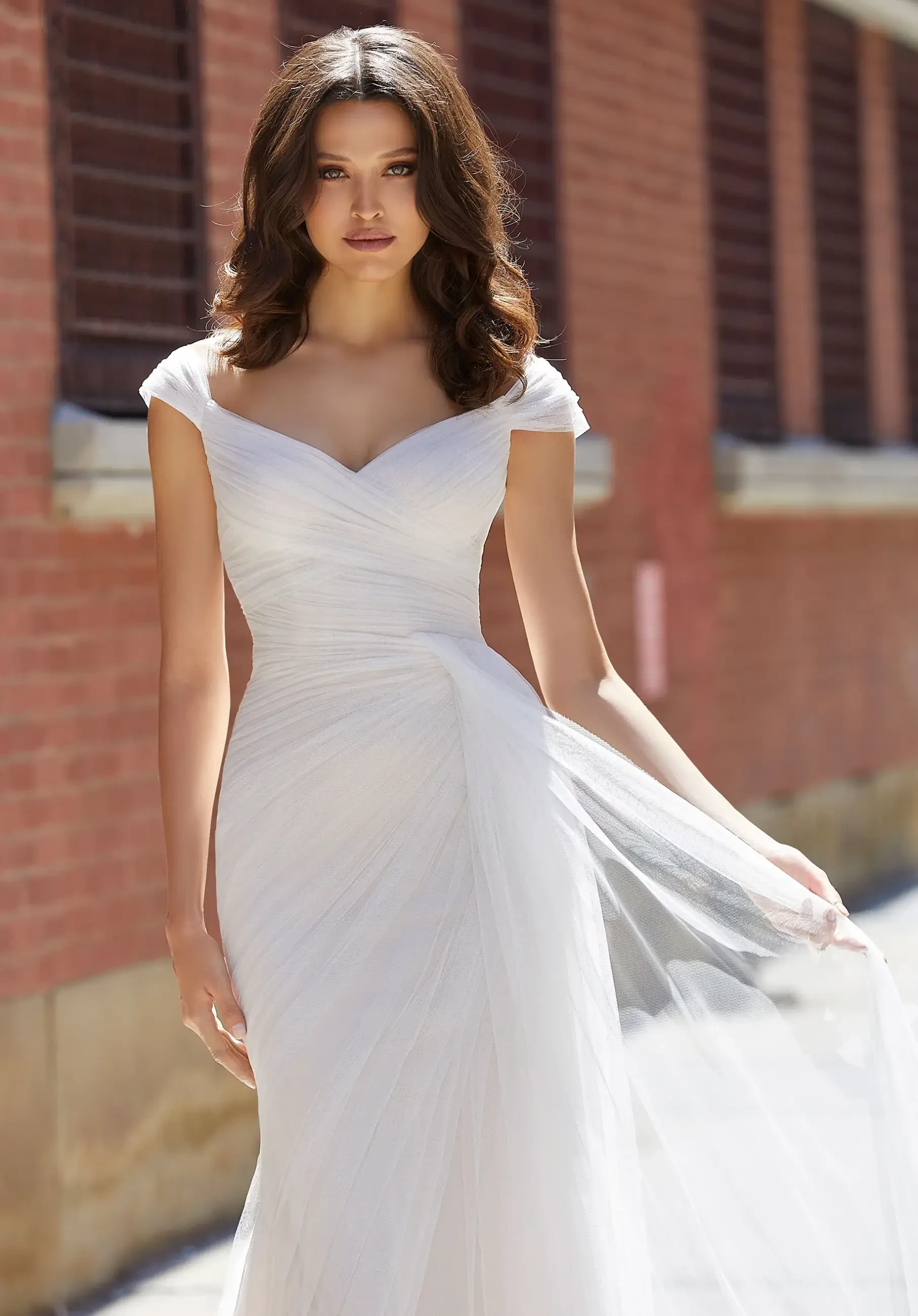 Model is wearing a fitted bridal gown with cap sleeves and a sweetheart neckline and ruching all over the gown