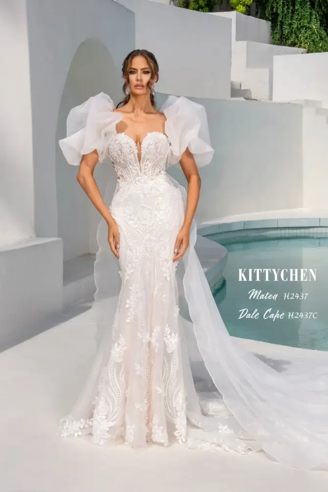 A woman in an elegant lace wedding gown with voluminous sleeves poses confidently. The backdrop features bright white architecture and a pool, conveying a serene and luxurious atmosphere.