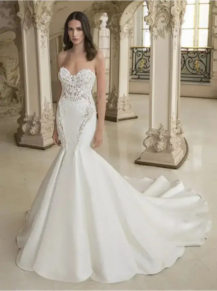 A woman in an elegant, strapless white wedding gown with lace detailing stands in a luxurious, ornate hall, exuding a graceful and sophisticated aura.